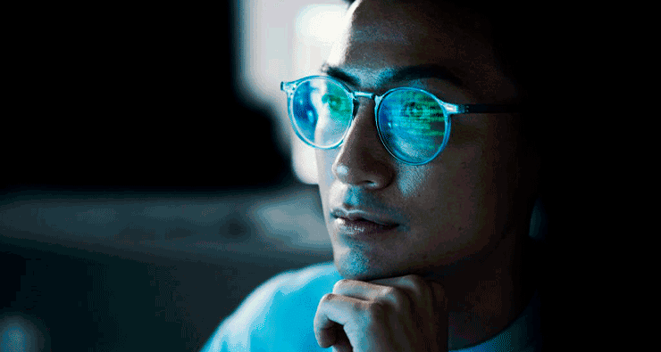 Um jovem de óculos olhando para a tela de um computador
