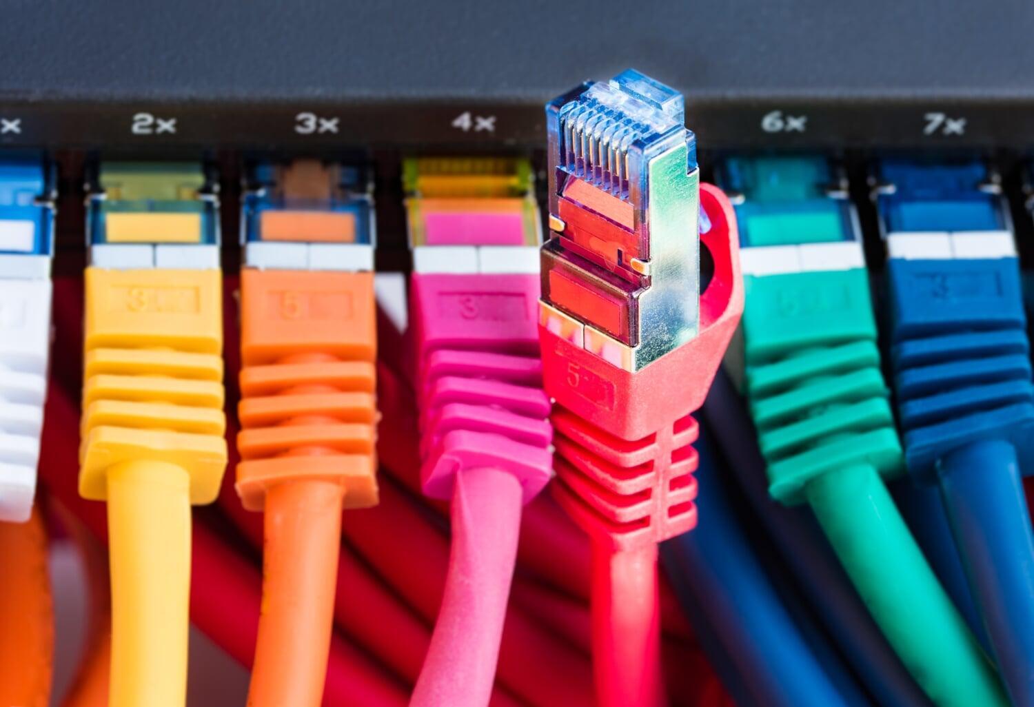 Conectores de rede coloridos ligados a switch, com um cabo desconectado em destaque