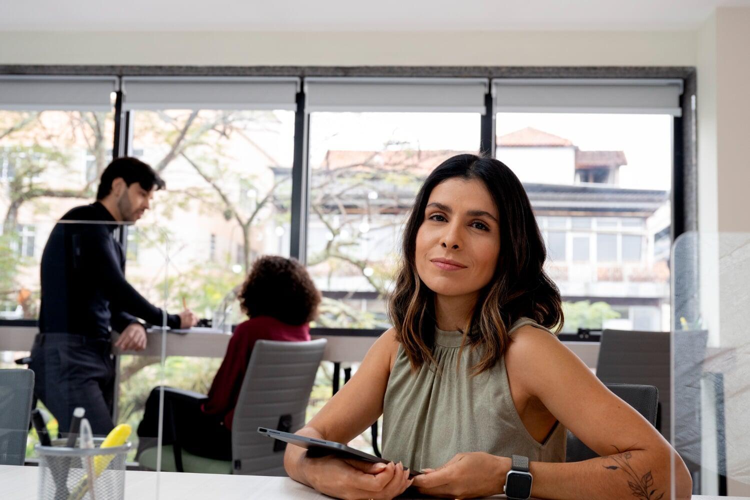 Mulher em reunião de trabalho com tablet nas mãos, sentada em sala envidraçada