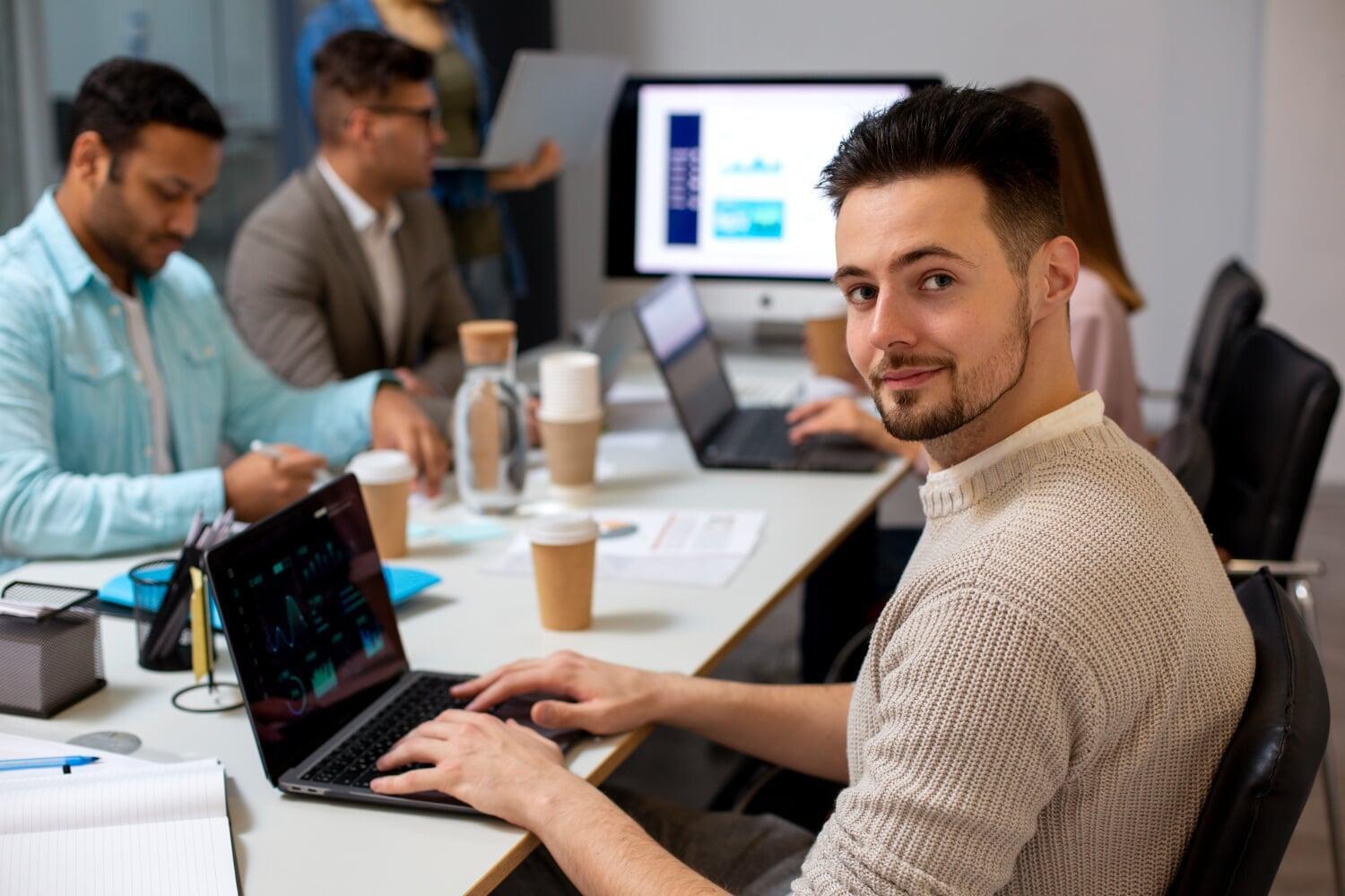 Profissional sorrindo em reunião com equipe, utilizando notebook para análise de dados empresariais