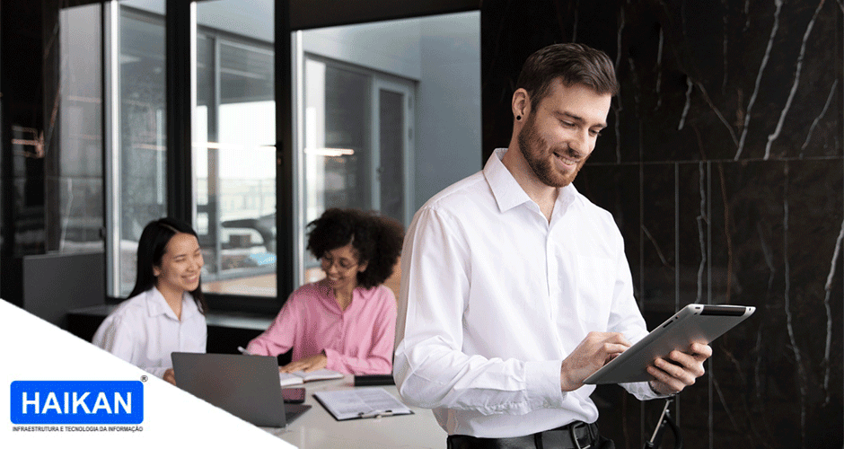Homem sorridente usando tablet em reunião corporativa moderna com colegas ao fundo