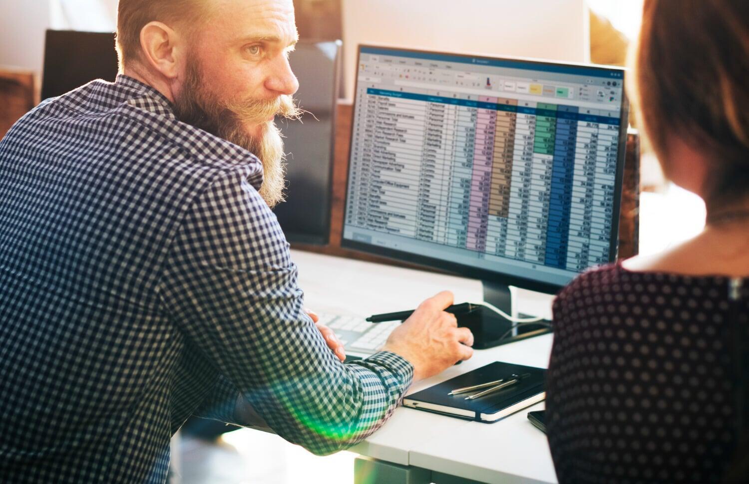 Técnico de tecnologia revisando planilha de dados em monitor de computador