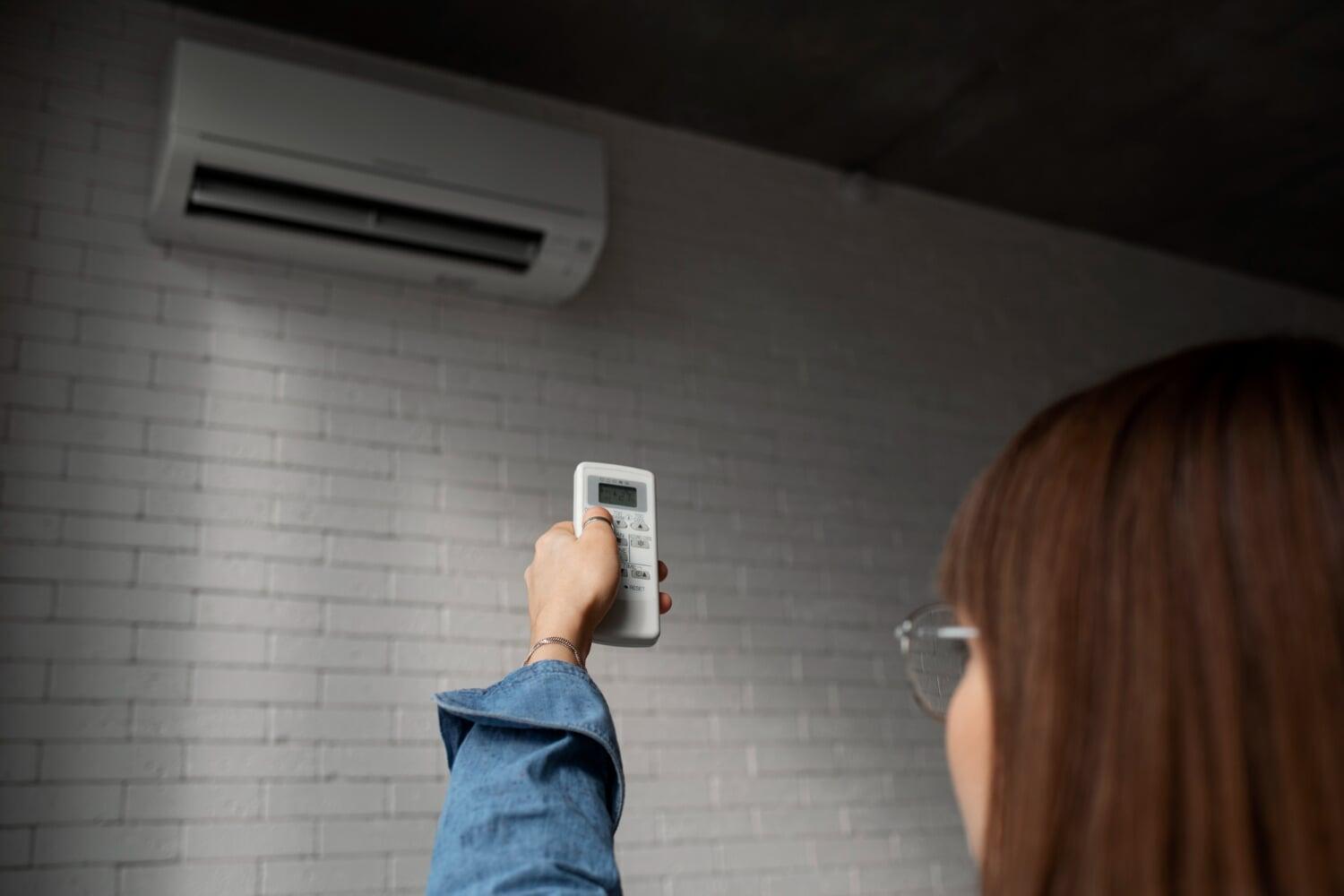 Pessoa apontando controle remoto para aparelho de ar-condicionado na parede
