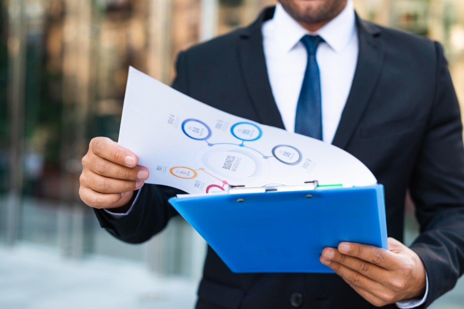 Profissional em traje social analisando relatório com infográfico de desempenho empresarial