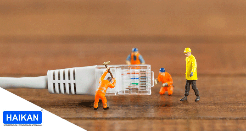 Miniaturas de operários em trajes de segurança trabalhando em um conector RJ45 sobre superfície de madeira